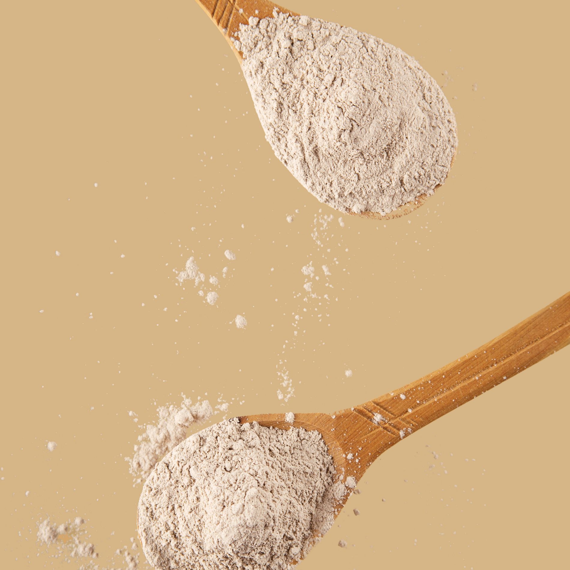 decorative image of tan powder on wooden spoons on tan background.