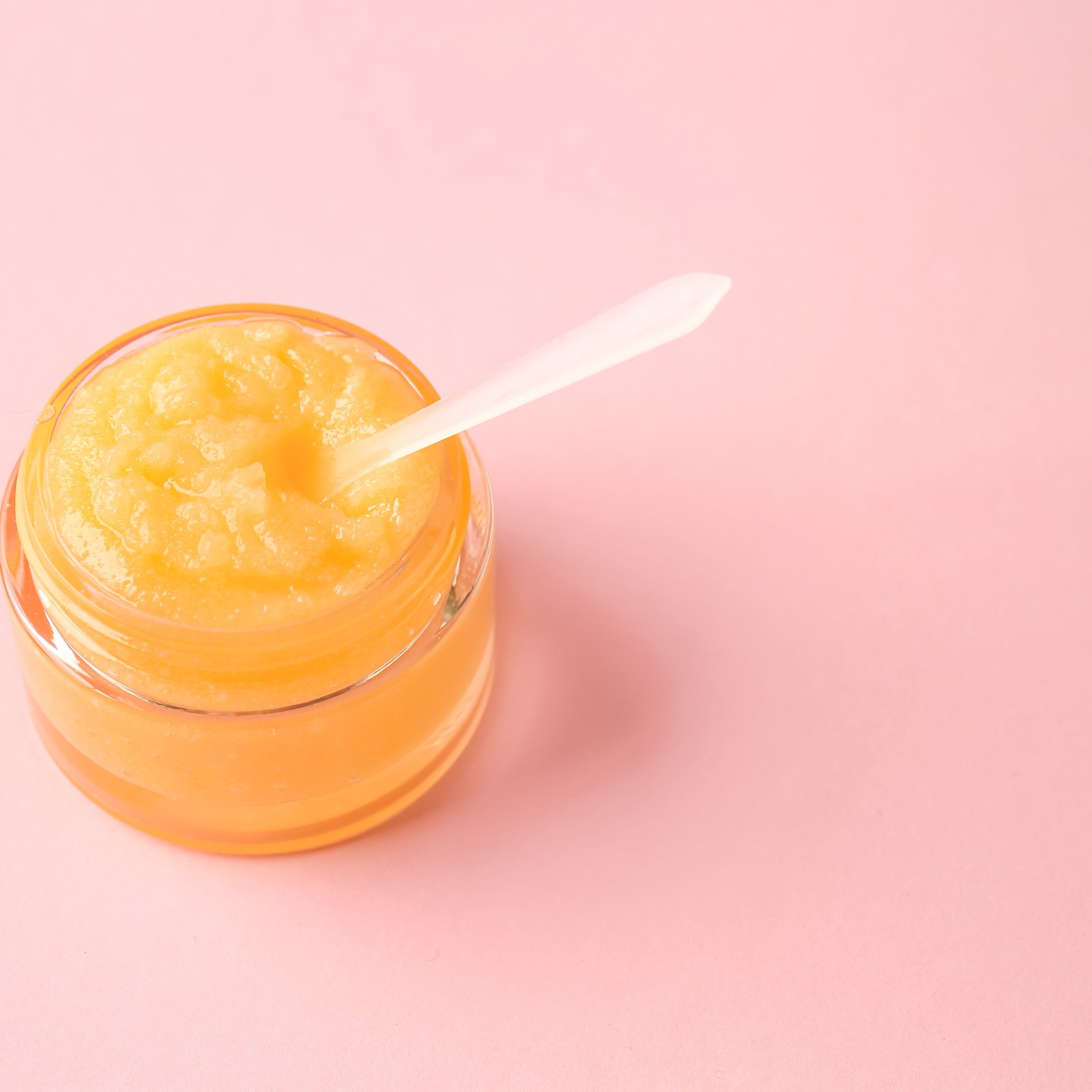 decorative image of orange sugar scrub with scoop on a pink background