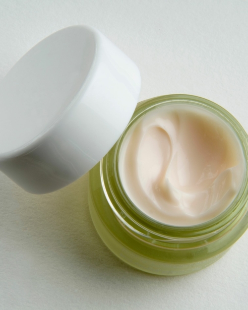 decorative image of face & body cream in a green jar with white background