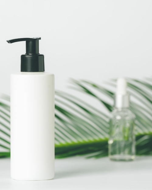 decorative image of Essential Jojoba Lotion with black pump and a palm leaf in the background